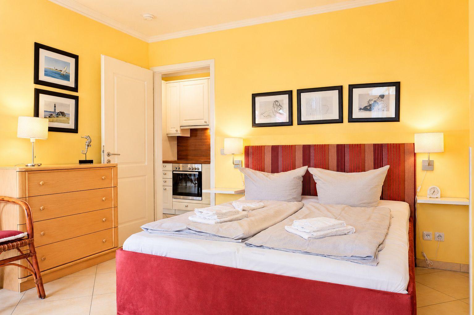 Schlafzimmer mit Bett, Schrank und Blick in die Küche.