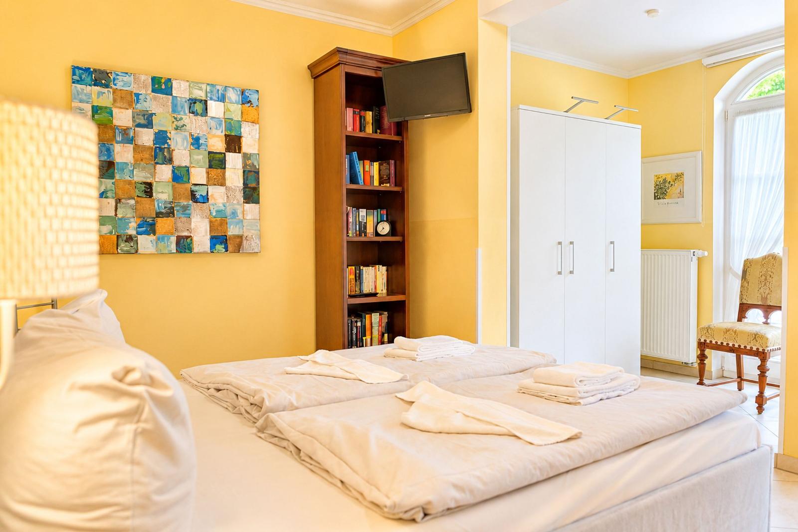 Schlafzimmer mit Bett, Bücherregal, Kleiderschrank und Fenster.