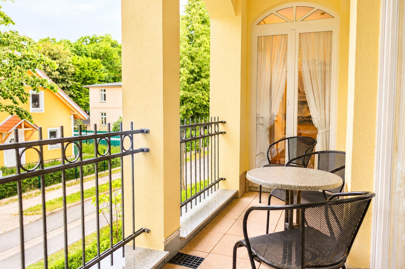 Terrasse mit Tisch und Stühlen, Blick auf grüne Umgebung und benachbarte Häuser.