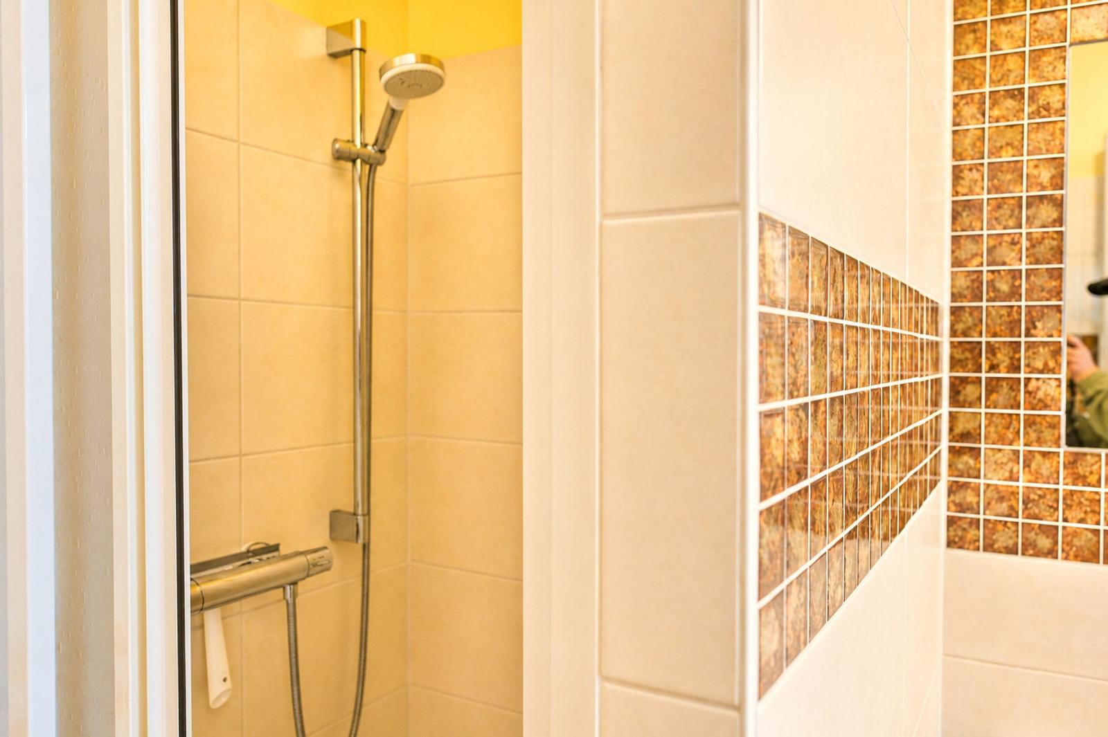 Dusche mit Duschbrause und Glaswand. Wand mit Mosaikfliesen.