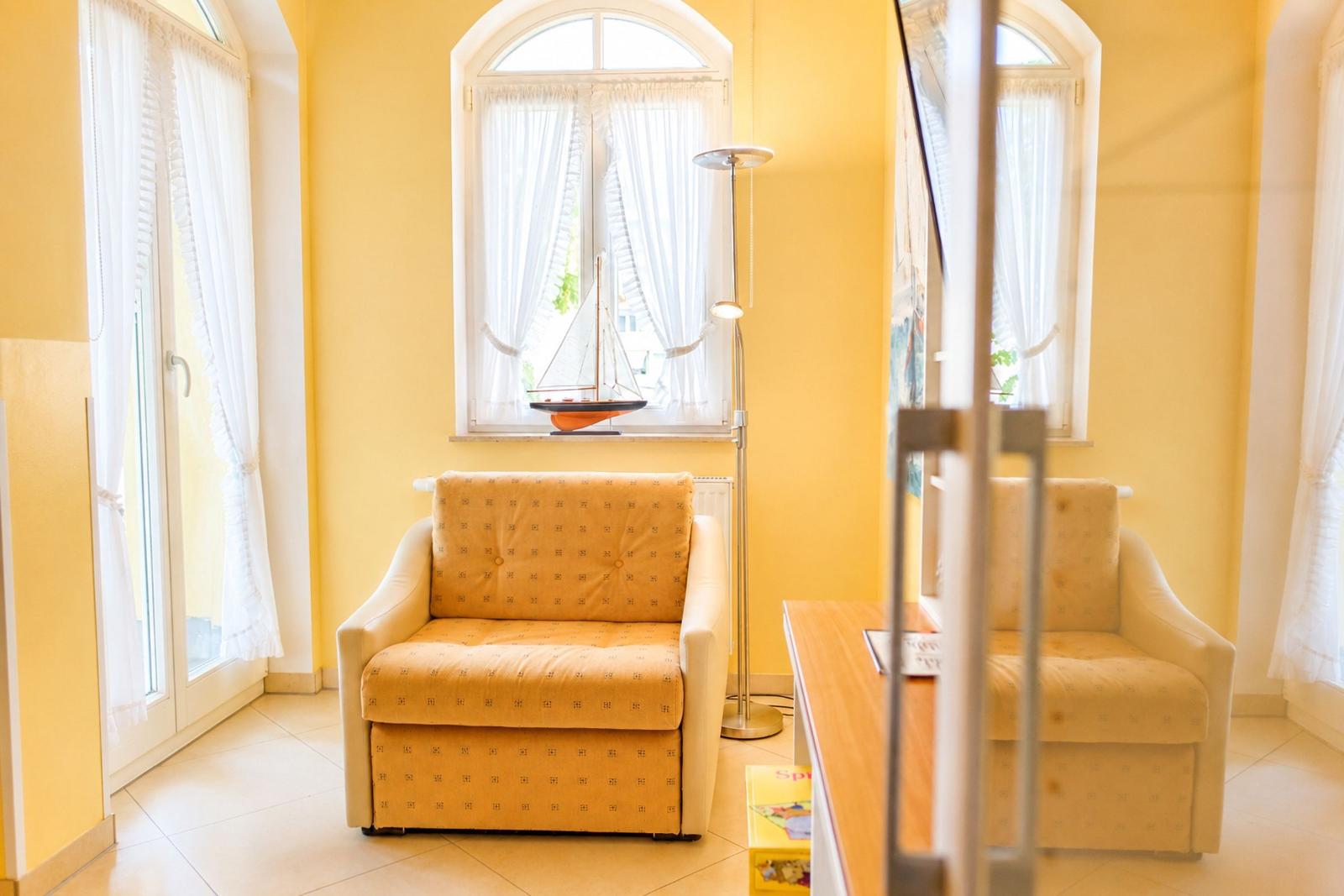 Ein Raum mit gelben Wänden, einem Sofa und einem Fenster mit Segelbootmodell.