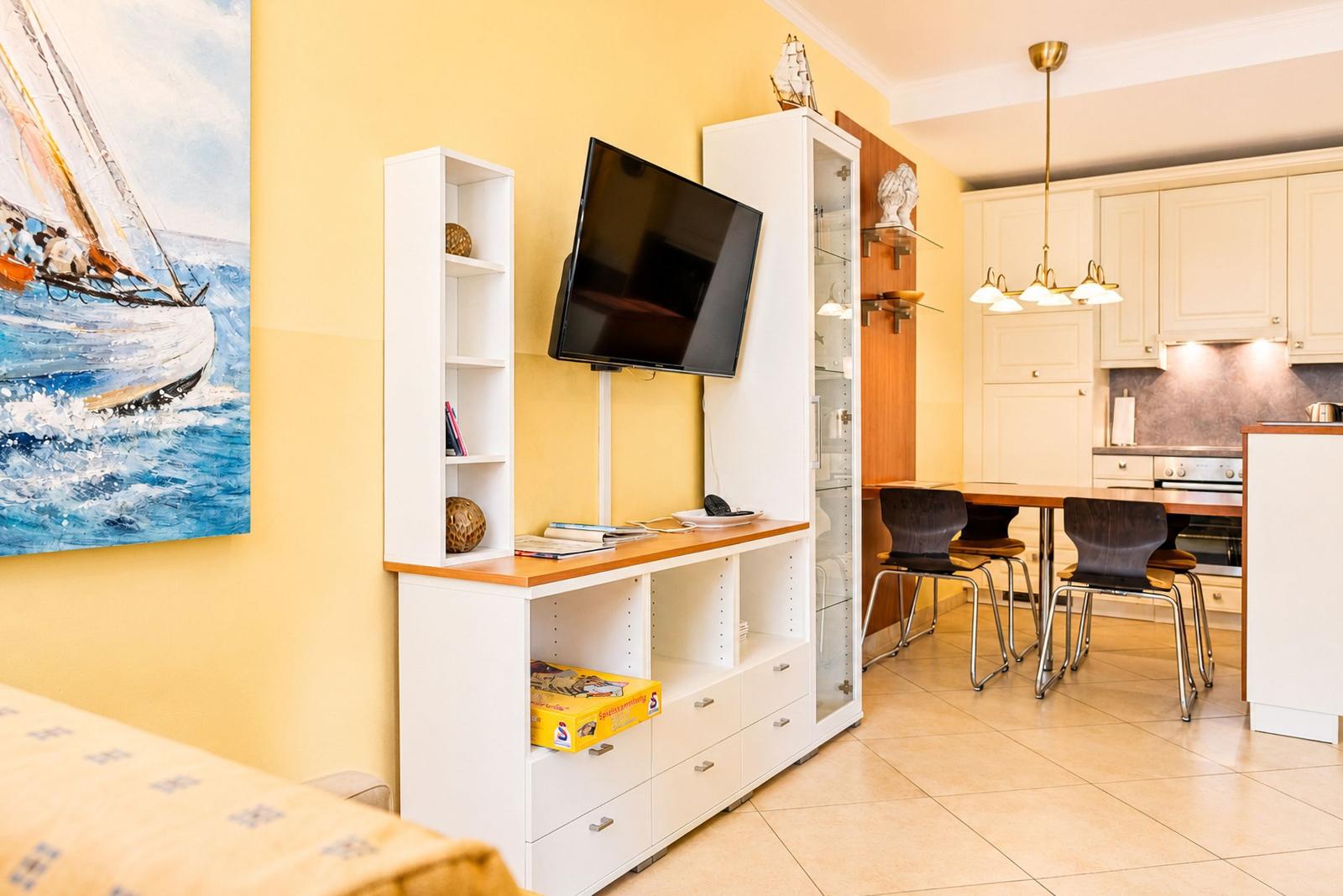 Wohn- und Essbereich mit Küchenzeile, TV und Wandbild mit Segelboot.