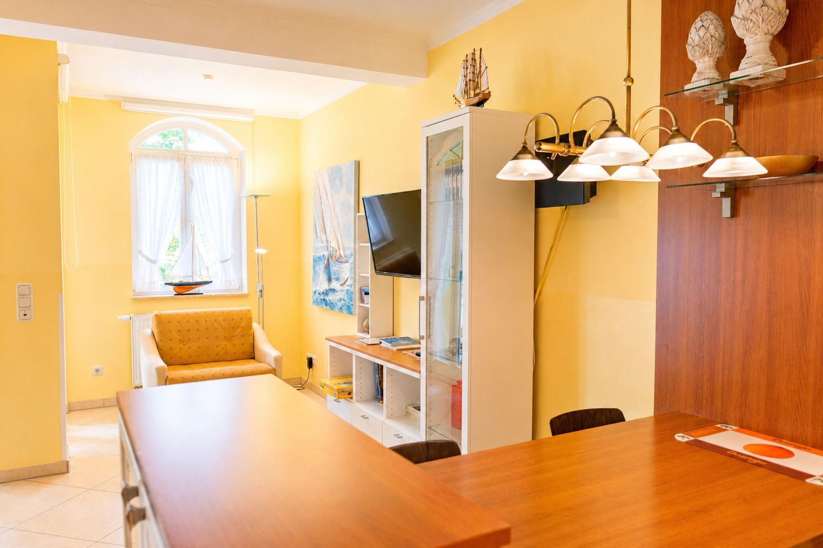 Wohn- und Essbereich mit Holztisch, gelben Wänden und Fernseher an der Wand.