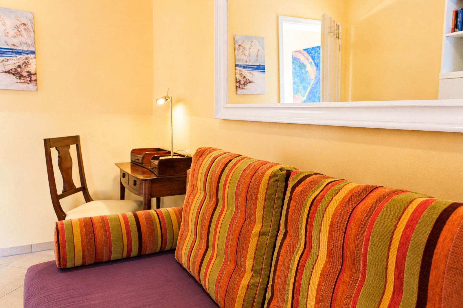 Sofa mit gestreiftem Kissen, Schreibtisch und Spiegel an der Wand.