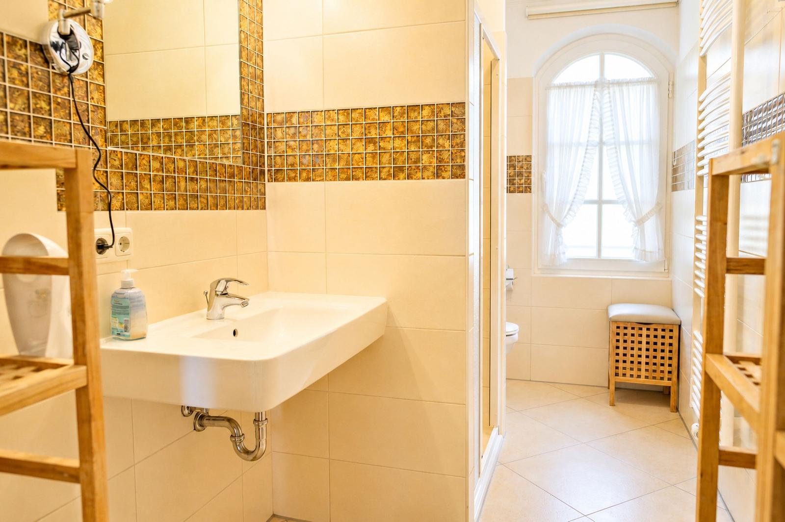 Bad mit Waschbecken, Spiegel, Dusche und Fenster mit Vorhängen.