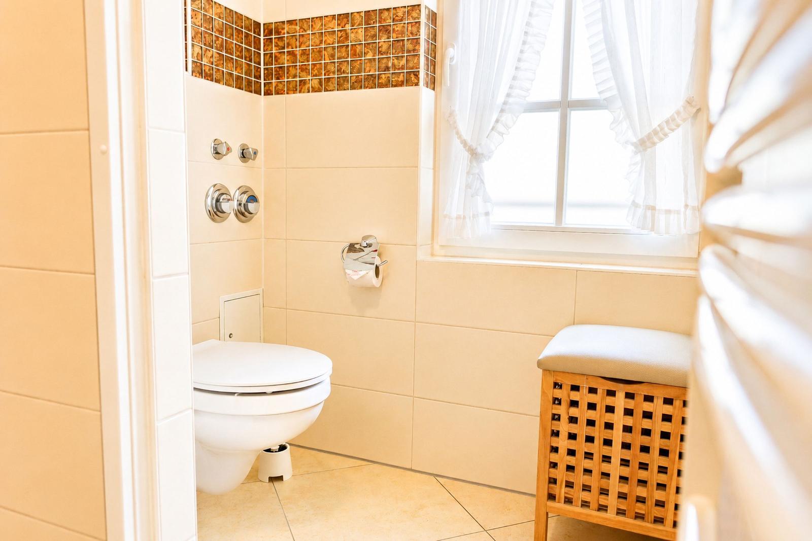 Badezimmer mit Toilette, Fenster und Holzbank mit Sitzkissen.