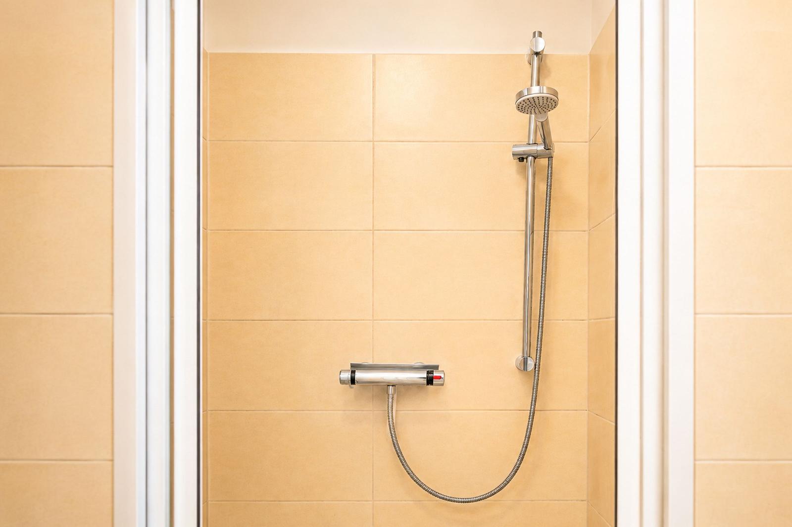 Dusche mit Handbrause und Temperaturregler an cremefarbenen Fliesen
