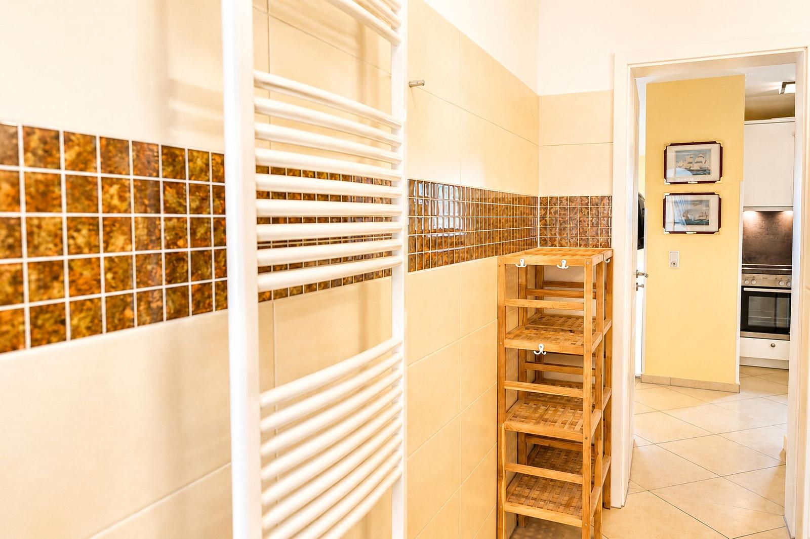 Flur mit Holzregal und Heizkörper, Wand mit Mosaikfliesen, Blick in die Küche.