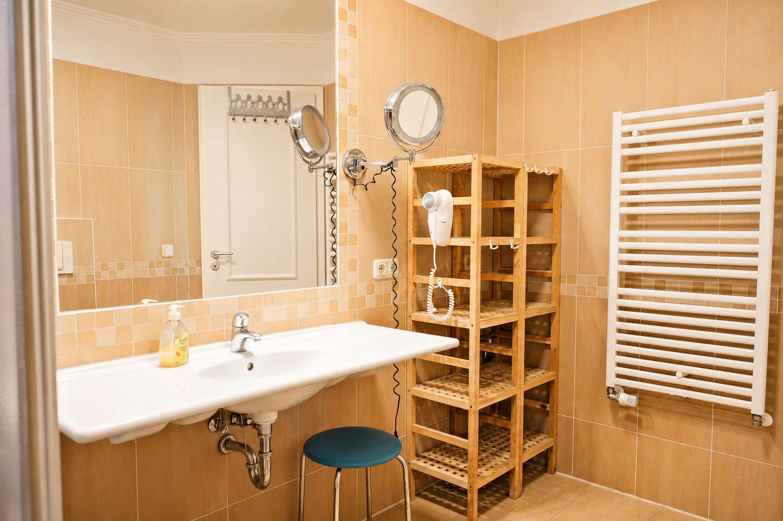 Badezimmer mit Waschbecken, Spiegel, Holzregal und Heizkörper.