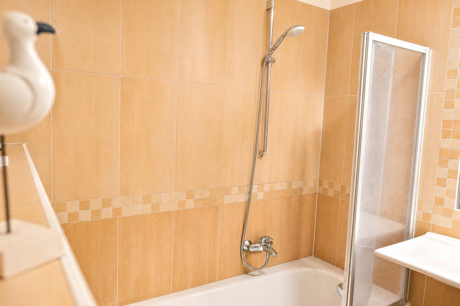 Bad mit Dusche, Badewanne und Waschbecken. Wandfliesen in beige.