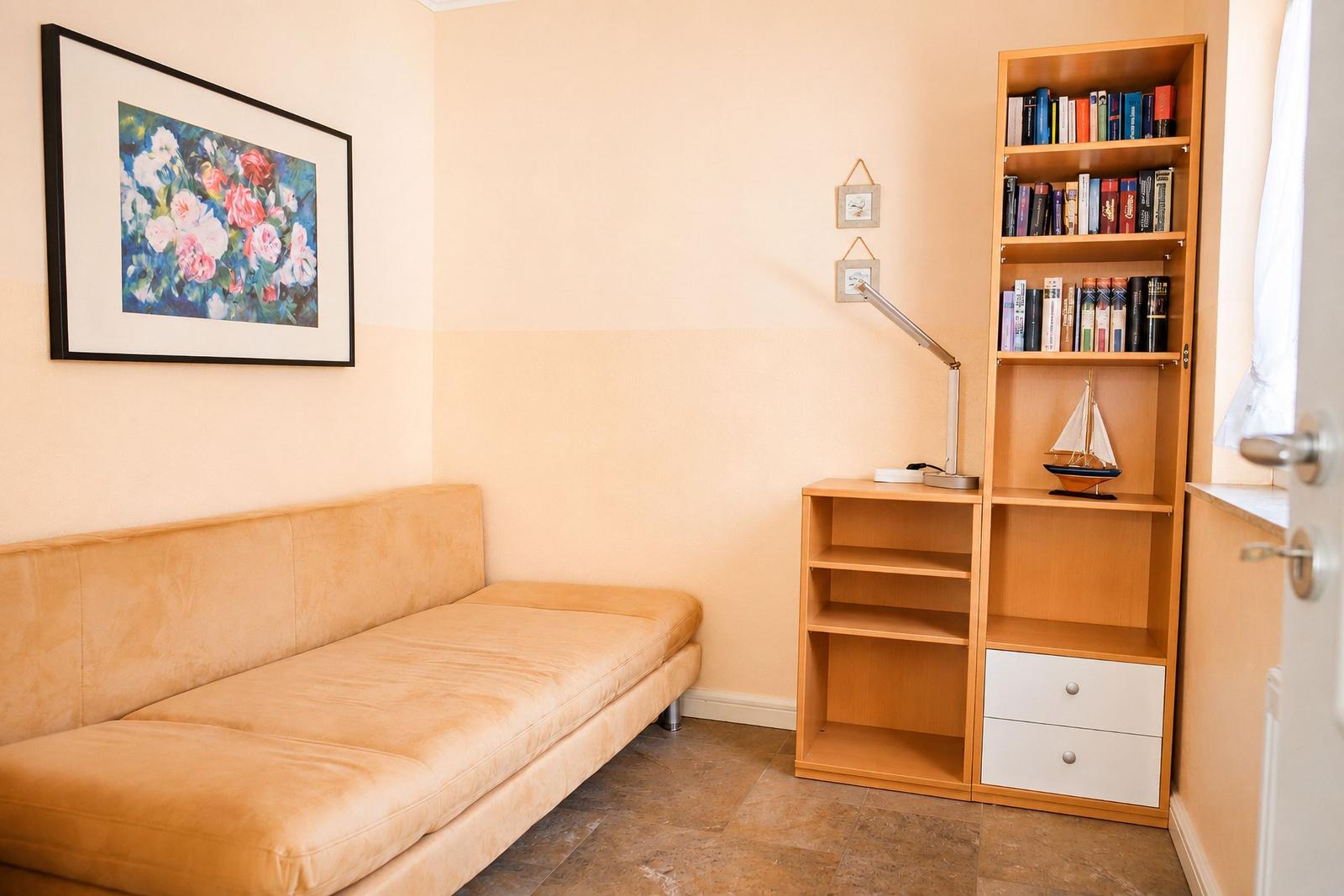 Ein Raum mit Sofa, Bücherregal und Wandbild mit Blumenmotiv.