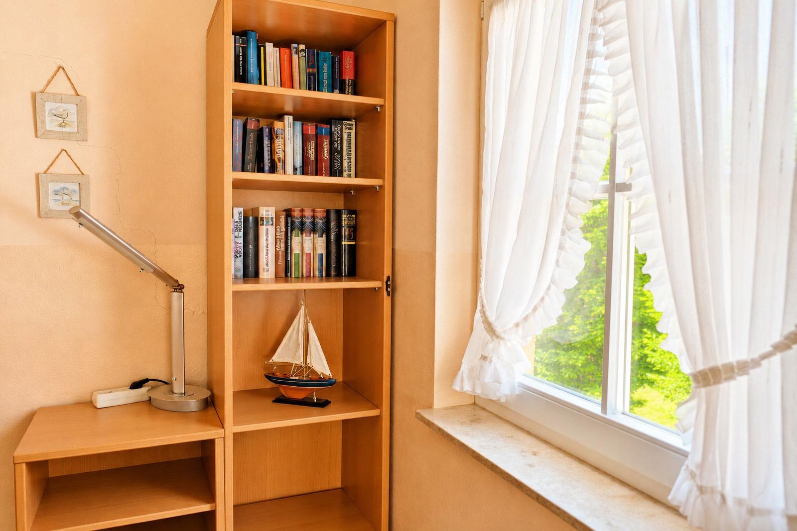 Bücherregal neben Fenster mit weißen Vorhängen und Segelschiffmodell