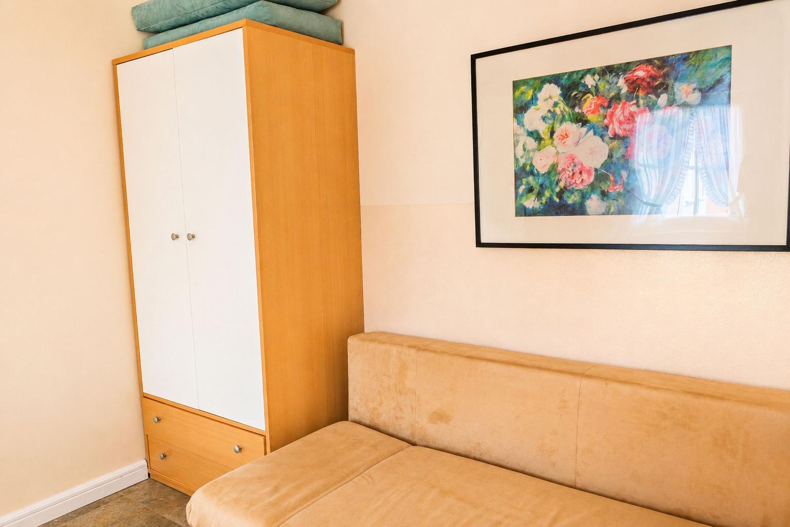 Schlafzimmer mit Kleiderschrank und Sofa. Wandbild mit Blumenmotiv.