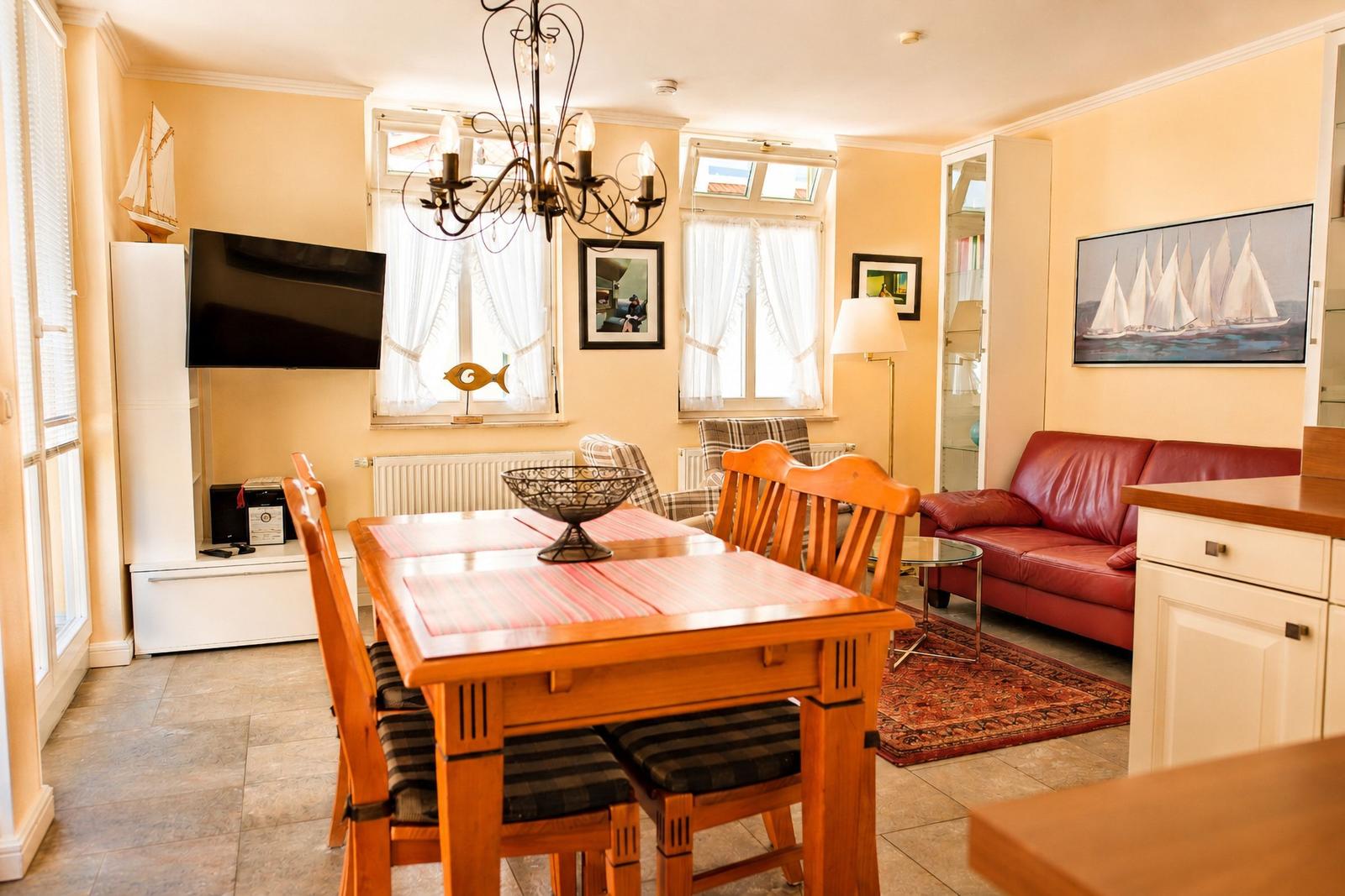 Esszimmer mit Holztisch, rotem Sofa und Wandbild mit Segelbooten.