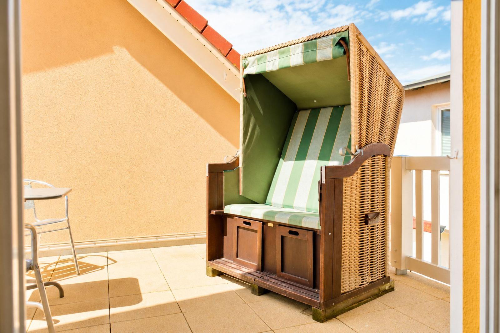 Terrasse mit Strandkorb, Tisch und Stühlen. Hintergrund: Wand und Himmel.