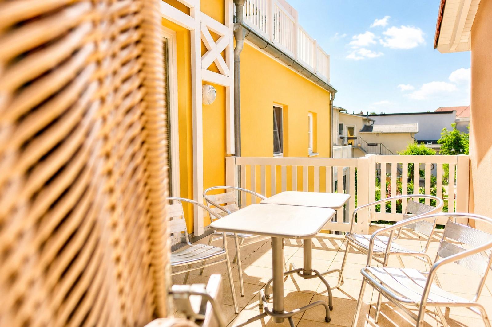 Terrasse mit Tisch und Stühlen vor gelbem Haus mit weißem Geländer.