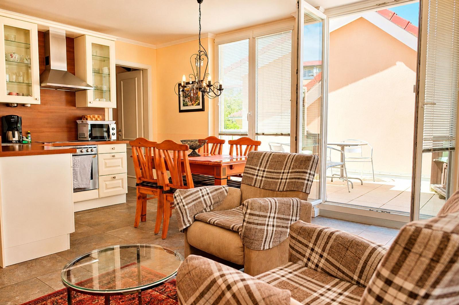 Küche, Essbereich und Wohnbereich mit Balkon. Möbel sind aus Holz und Stoff.