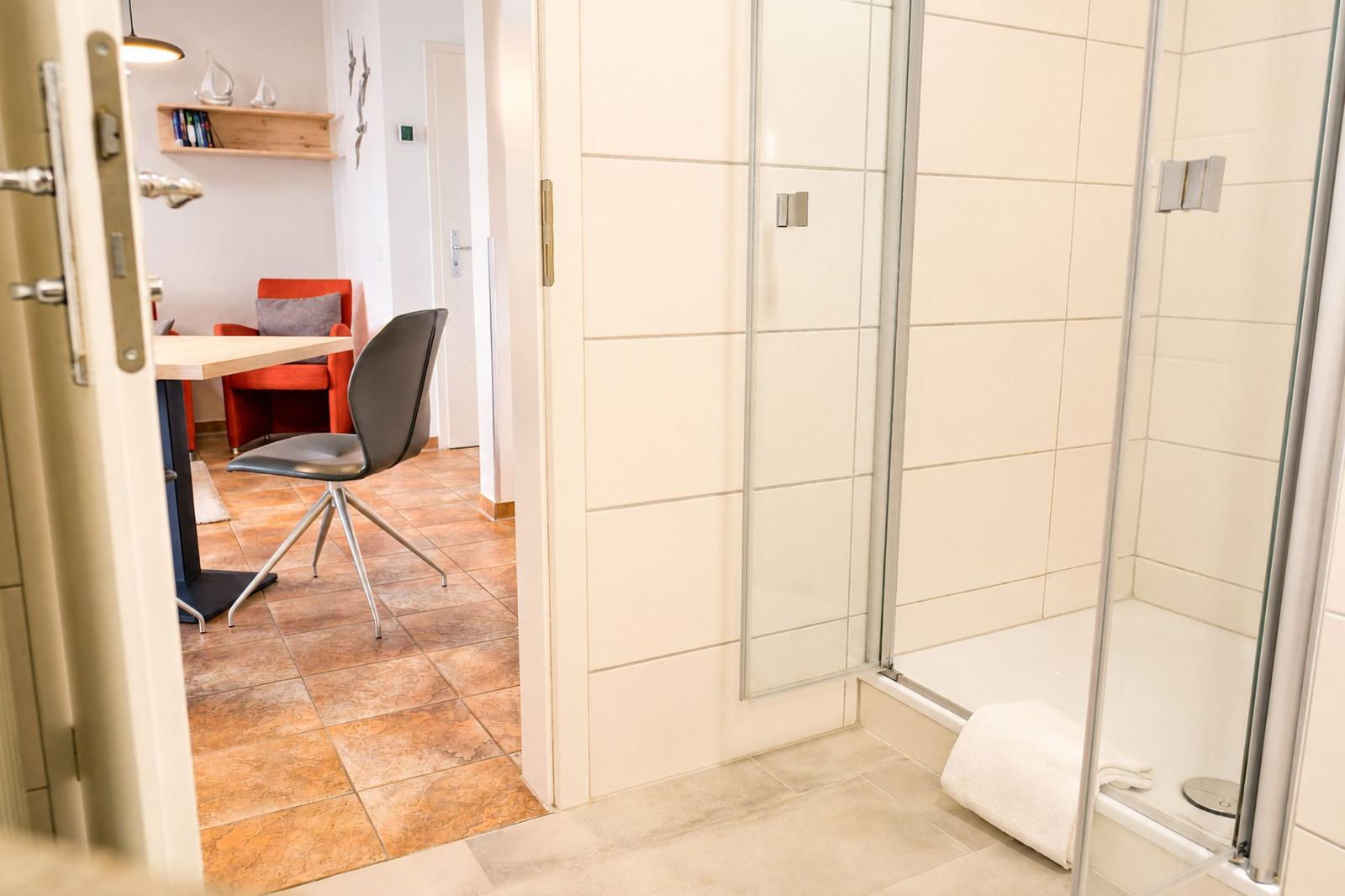 Badezimmer mit Dusche und Blick in Wohnbereich mit Tisch und Stühlen.
