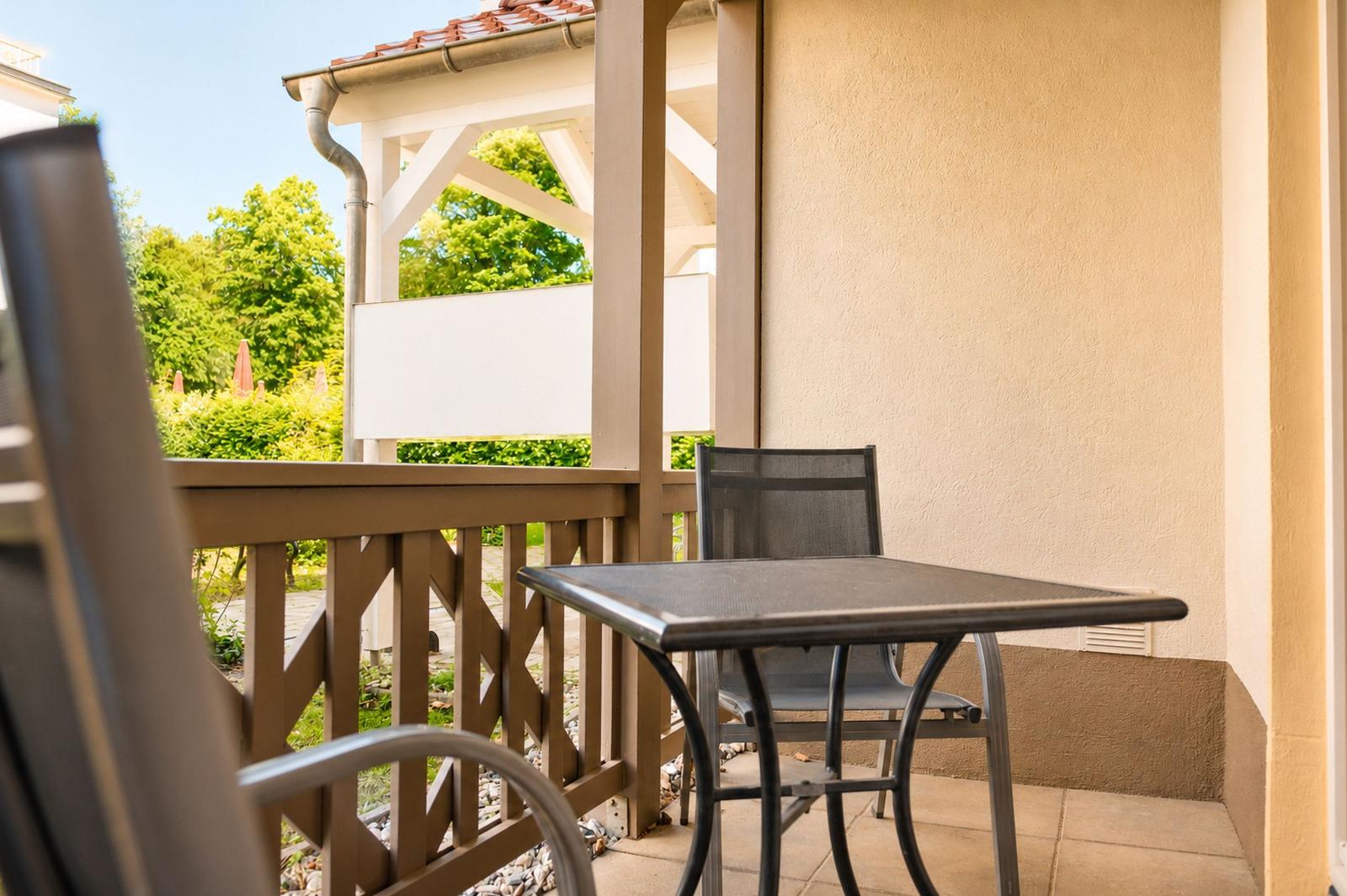 Terrasse mit Tisch und Stühlen, Blick auf grüne Bäume und einen Pavillon.