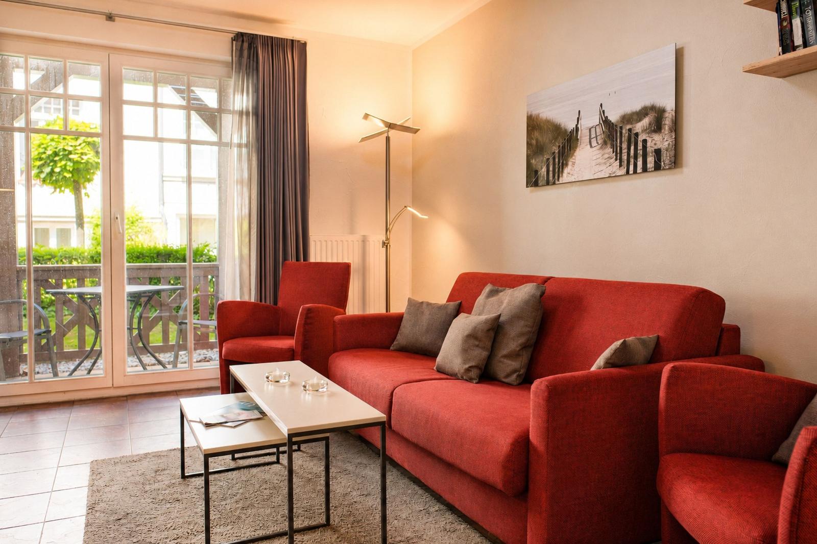 Ein Wohnzimmer mit rotem Sofa, Sitzgelegenheiten und Blick auf einen Balkon.