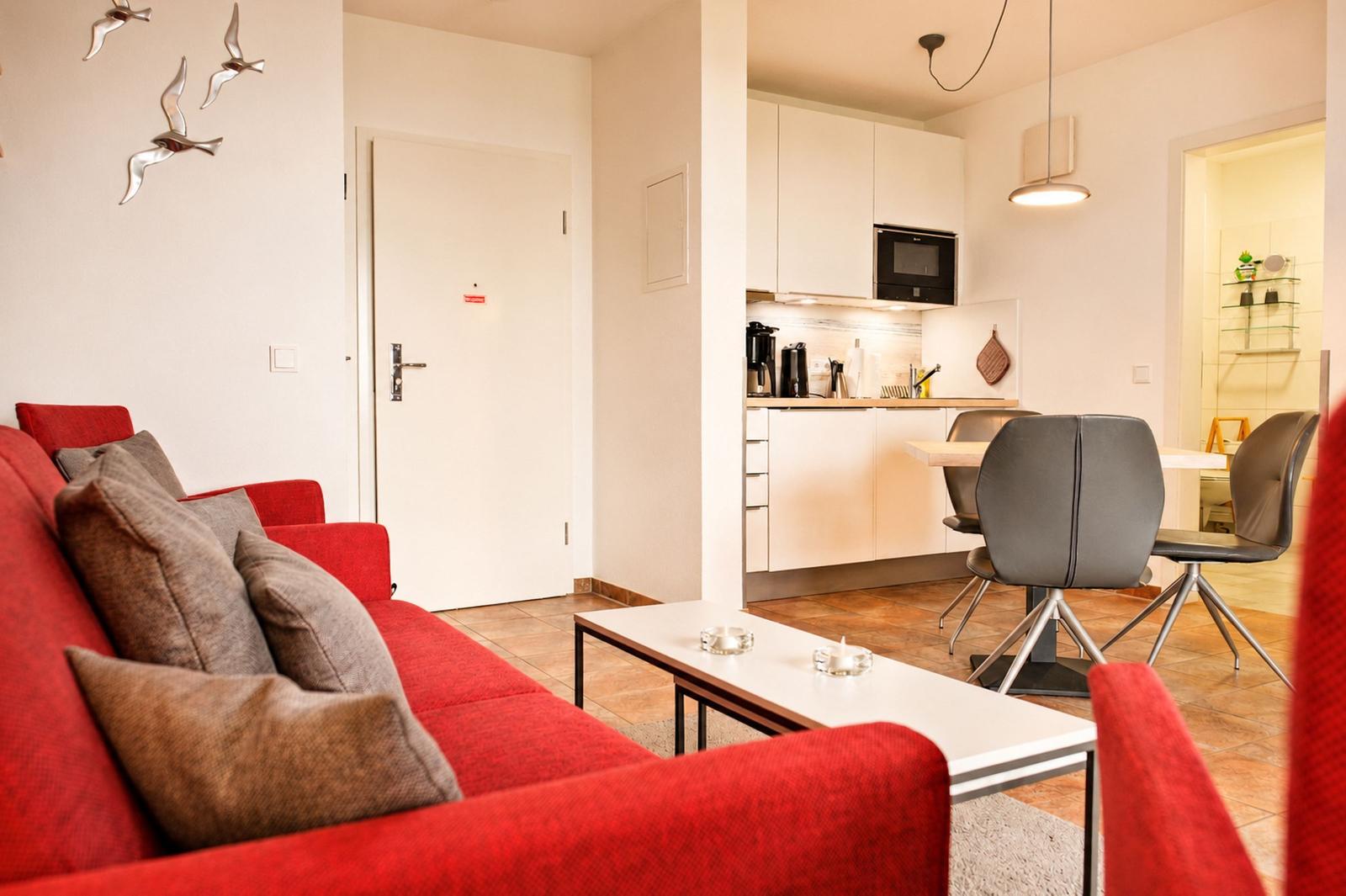 Wohnbereich mit rotem Sofa, Küchenbereich und Essplatz mit grauen Stühlen.