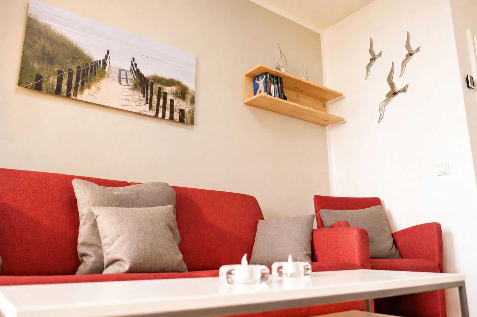 Rotes Sofa mit Kissen, Wandbild und Regal mit Büchern