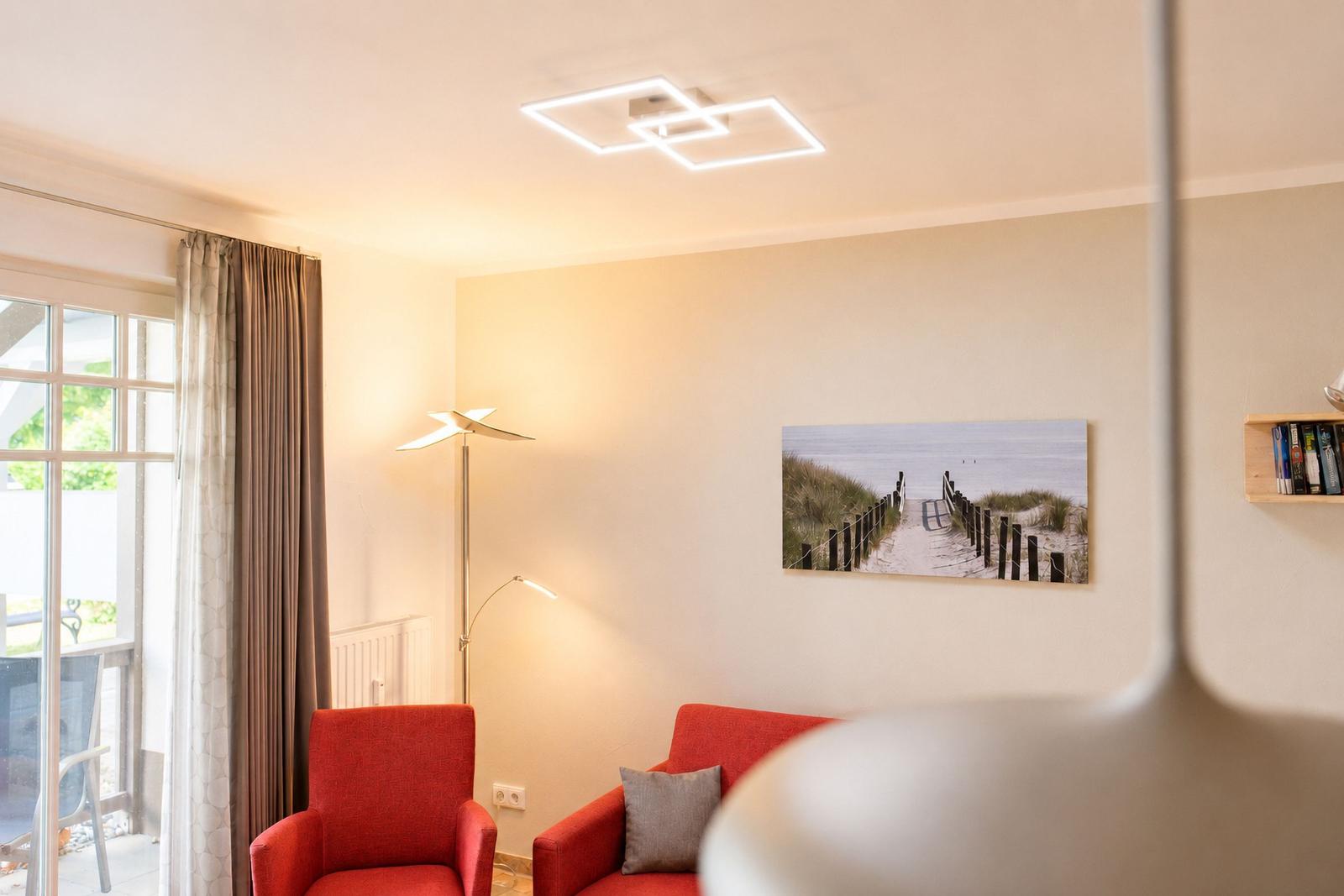 Ein Wohnzimmer mit roten Sesseln, Wandbild und Bodenheizung.