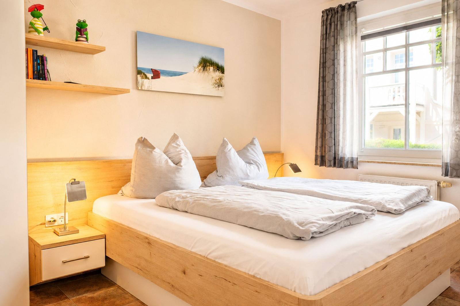Schlafzimmer mit Holzbett, Nachttisch und Wandbild. Fenster mit Vorhängen.