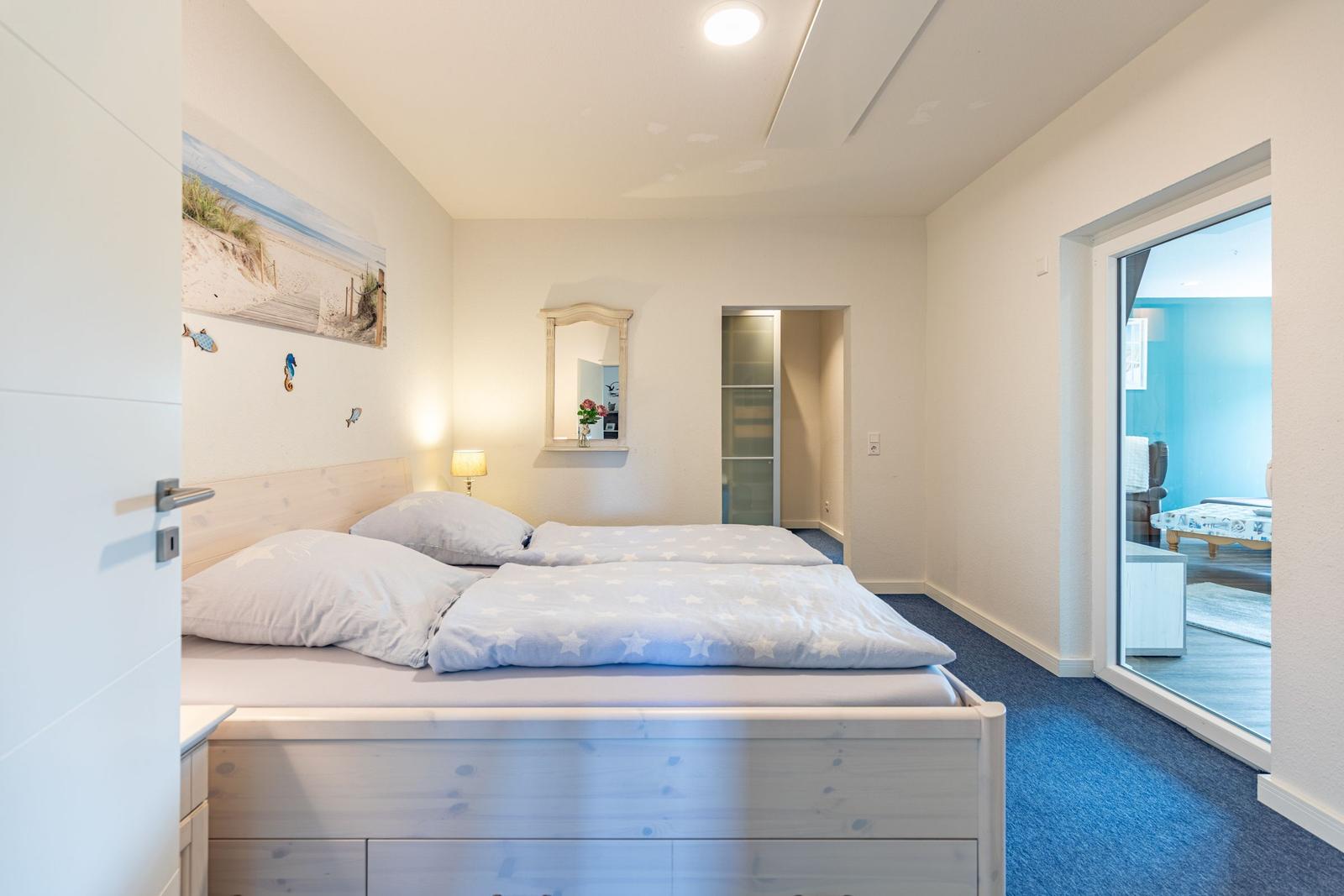 Schlafzimmer mit Doppelbett, Wandbild und Blick in angrenzenden Raum.