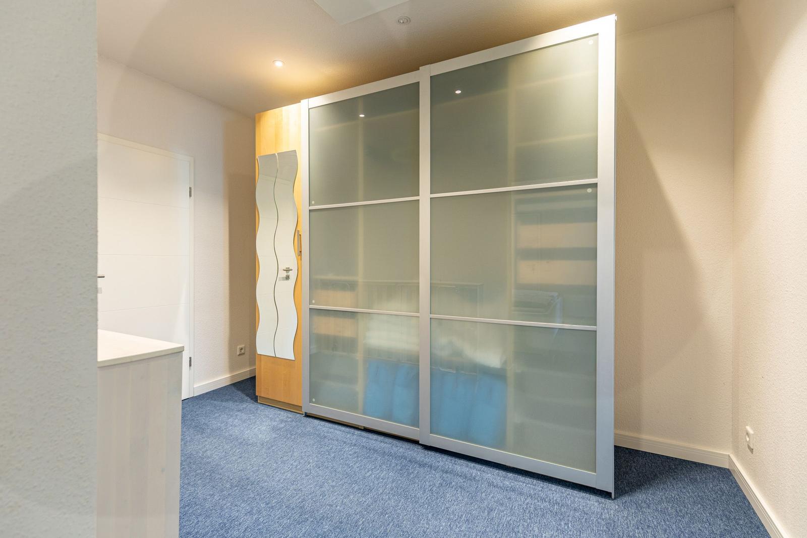 Schlafzimmer mit Schiebetüren-Schrank und blauem Teppichboden.