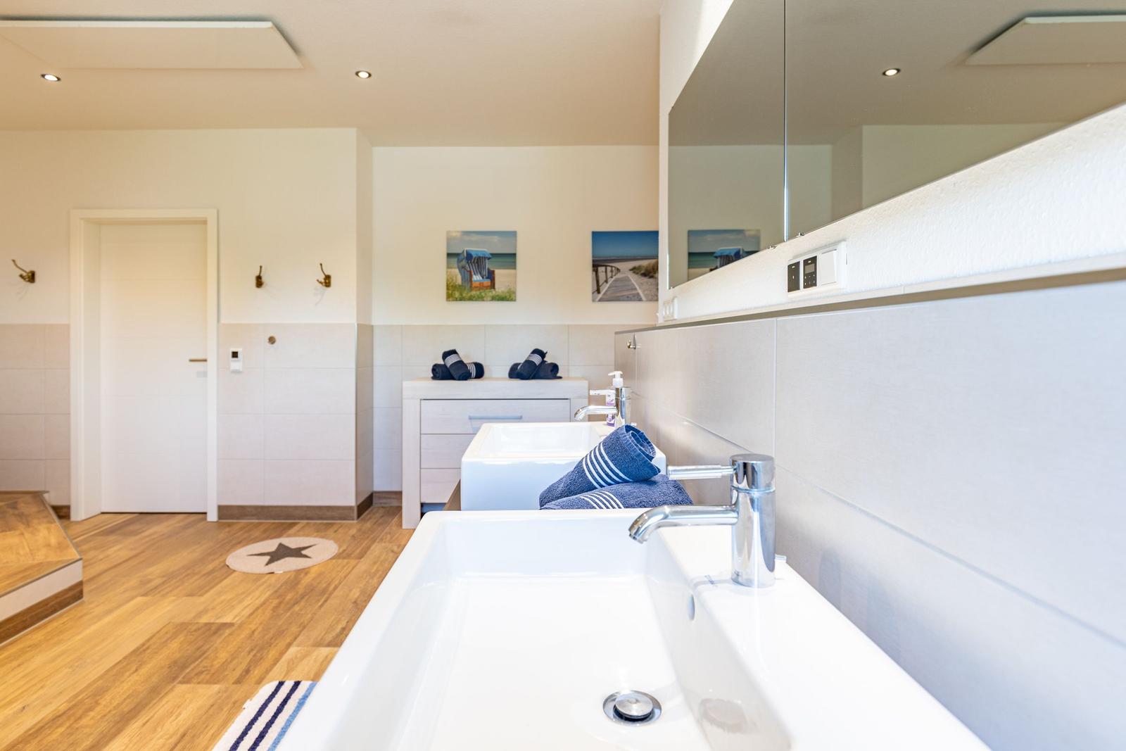 Badezimmer mit zwei Waschbecken, Spiegelschrank und Strandmotivbildern an der Wand.