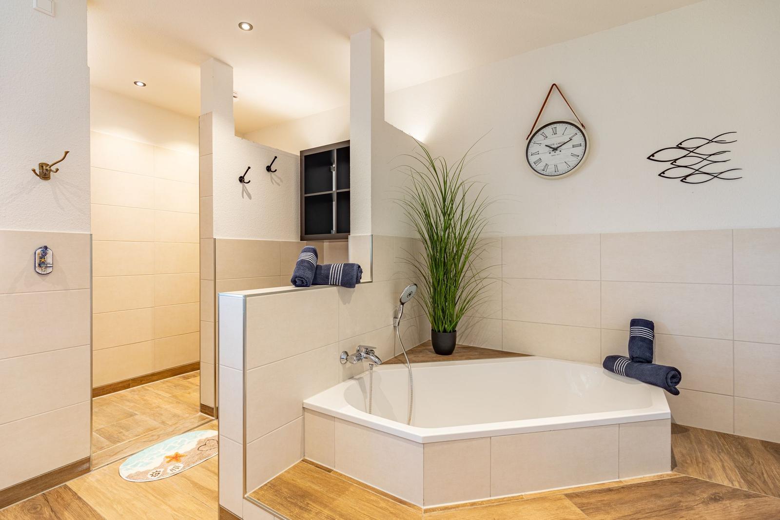 Bad mit Badewanne, Dusche und Pflanze. Wanduhr und Handtücher sind sichtbar.