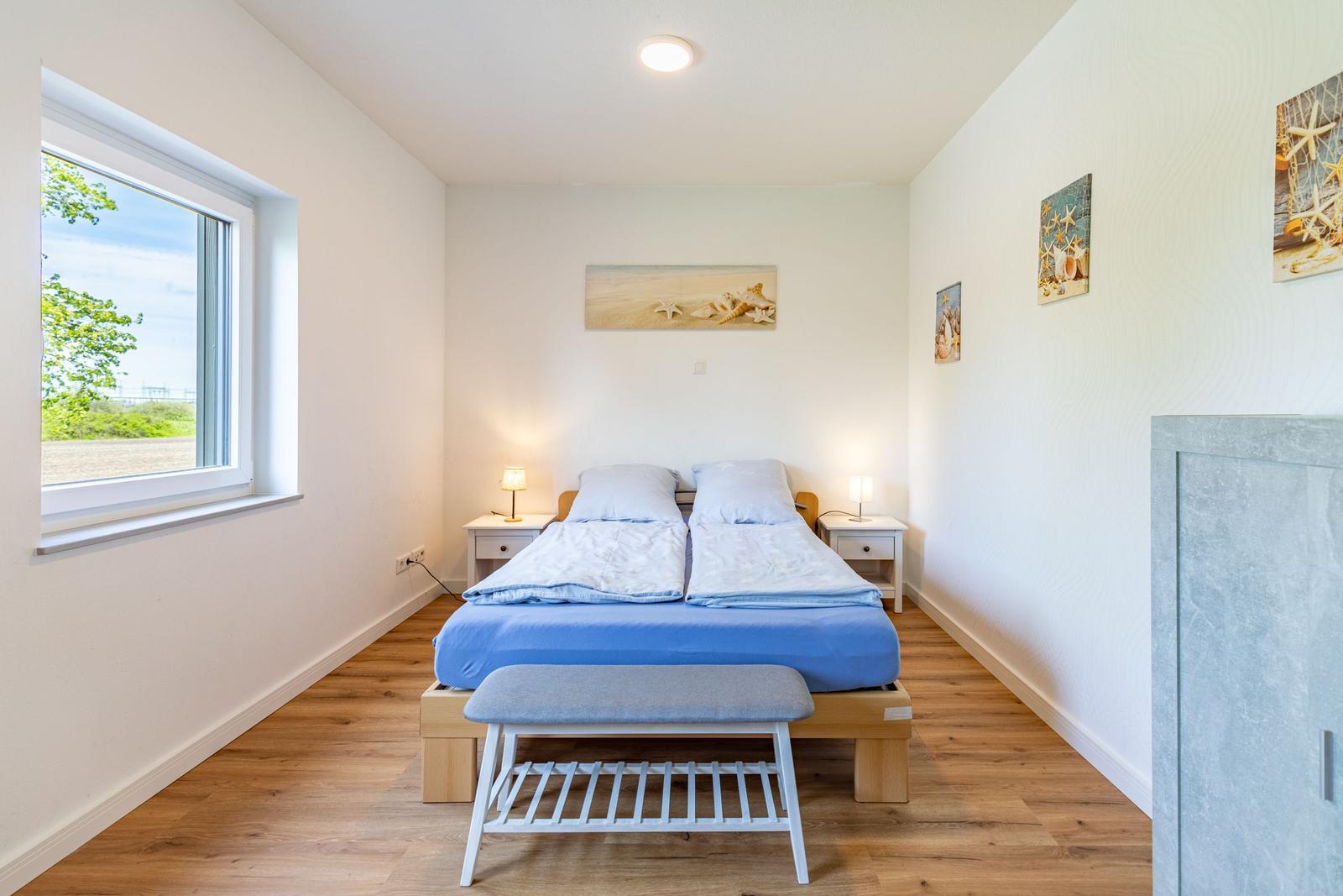 Schlafzimmer mit Doppelbett, Fenster und Strandmotiven an den Wänden.
