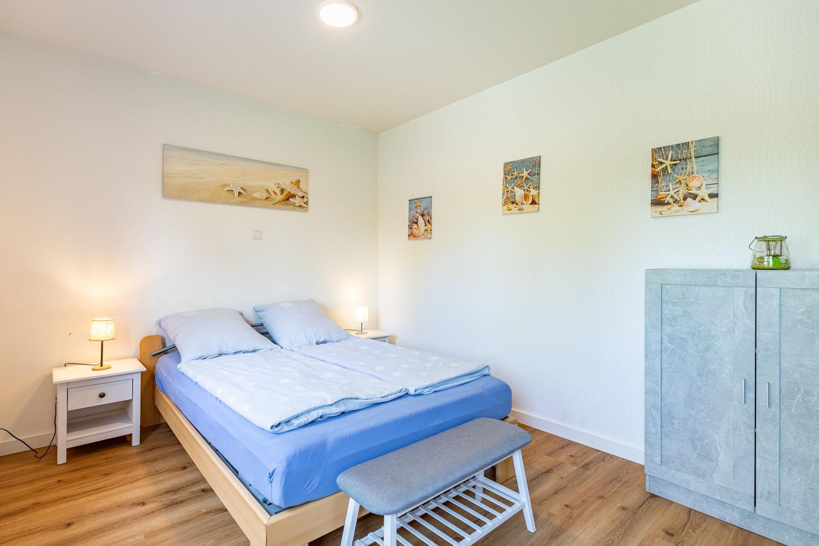 Schlafzimmer mit Bett, Nachttischen und Kleiderschrank. Wandbilder mit Meeresmotiven.