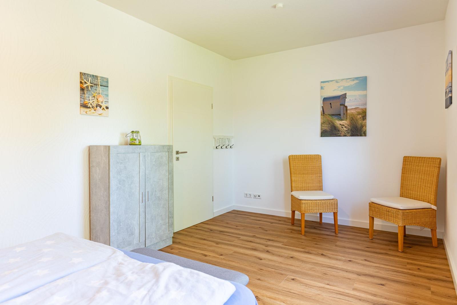 Schlafzimmer mit Bett, Kleiderschrank, zwei Stühlen und Wandbildern.