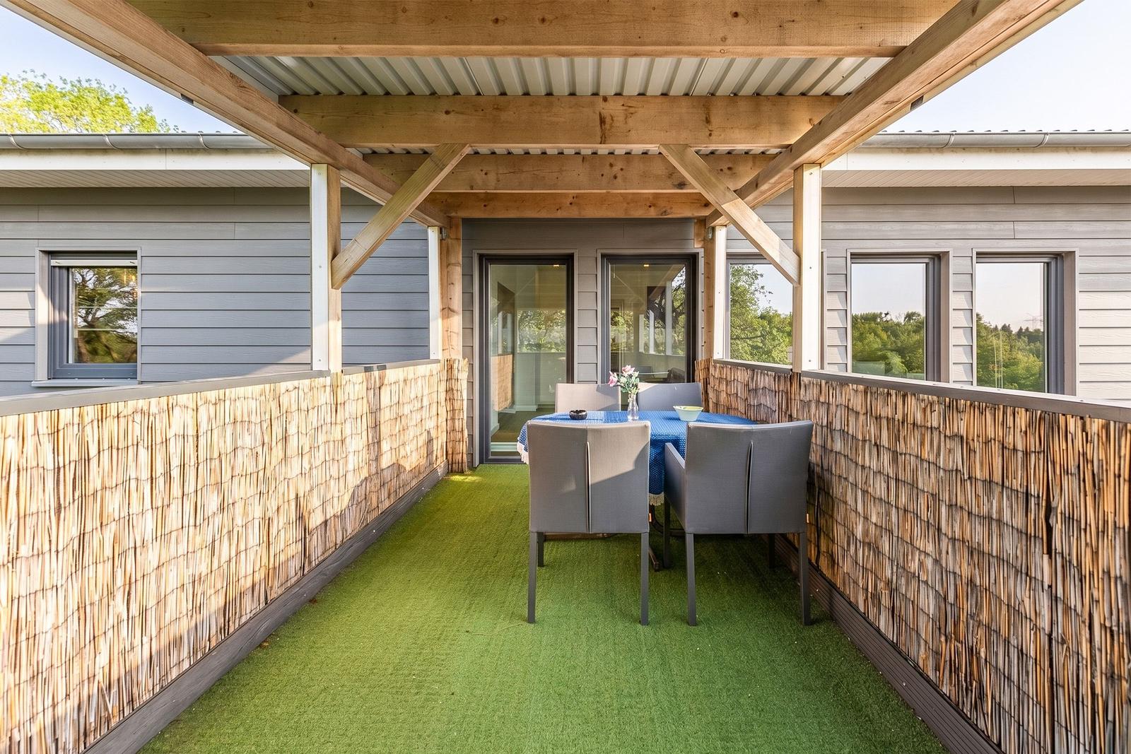 Terrasse mit Sitzgruppe, grünem Kunstgras und Holzüberdachung.
