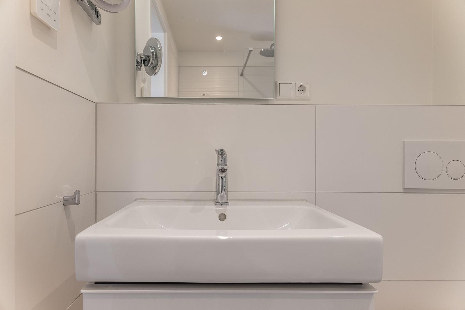 Waschbecken mit Spiegel und Wasserhahn in einem hellen Badezimmer.