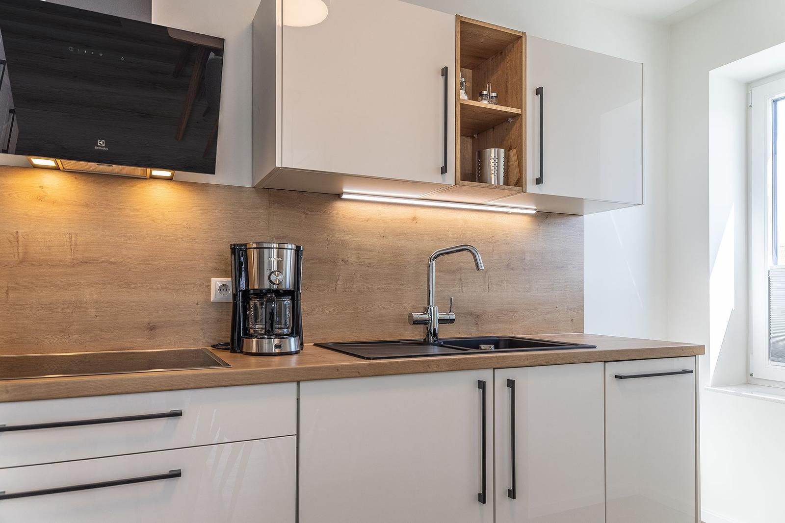 Moderne Küche mit weißen Schränken, Holzrückwand und Edelstahlspüle.