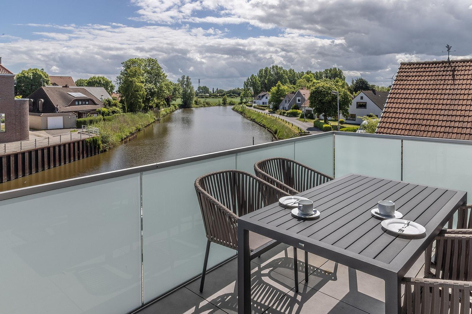 Terrasse mit Tisch und Stühlen, Blick auf einen Kanal und Wohnhäuser.