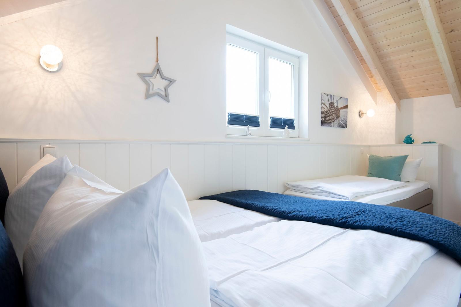 Zwei Betten mit weißen Laken und blauen Decken unter einem Holzdach
