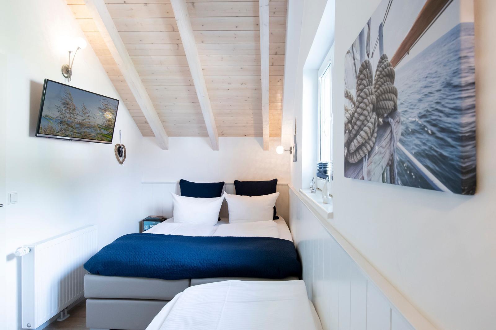 Schlafzimmer mit Bett, Fernseher und Wandbild an der Seite.
