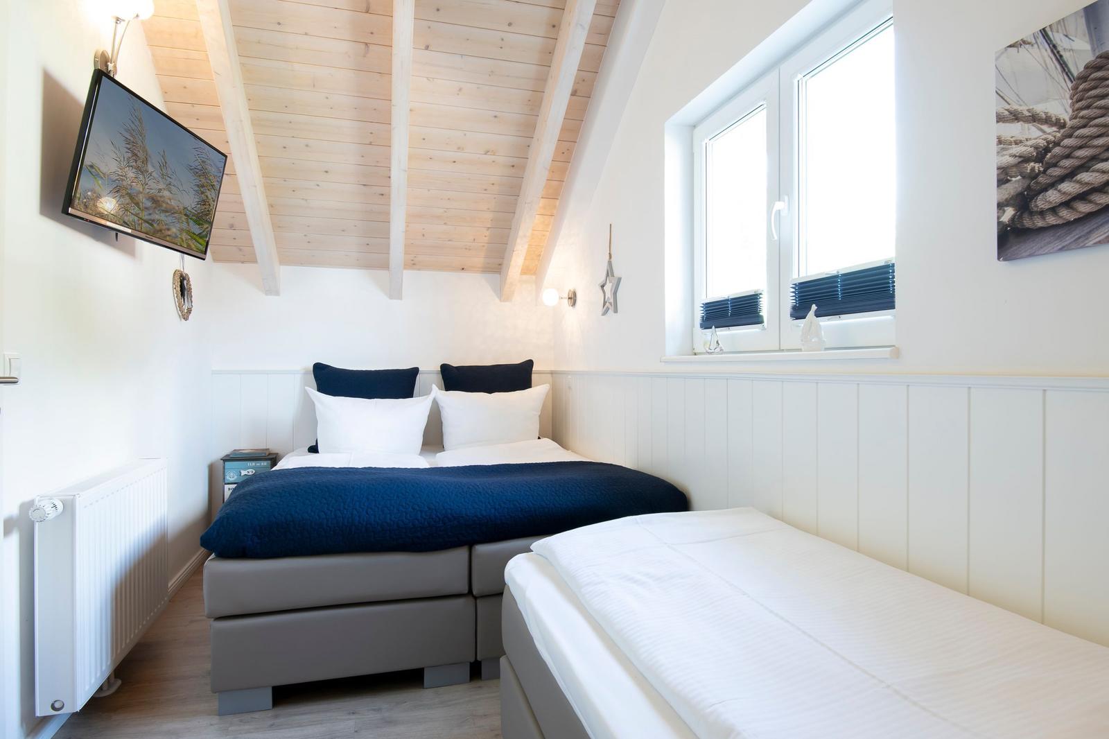 Zimmer mit Doppelbett, Einzelbett, Fenster und TV an der Wand.