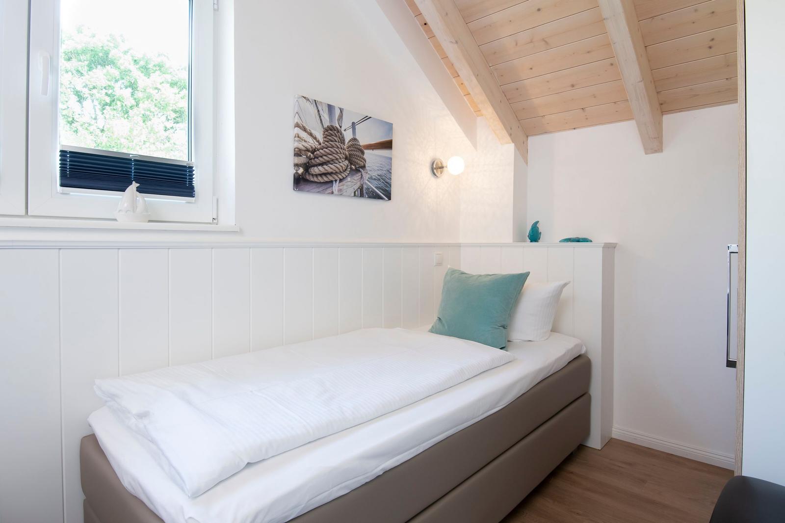 Schlafzimmer mit Einzelbett, Fenster und Holzdecke.