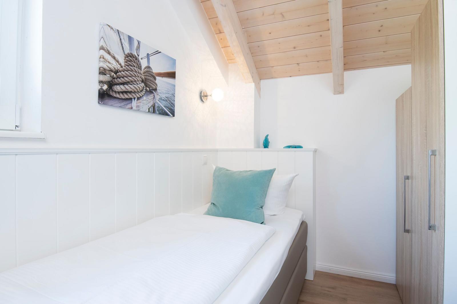 Schlafzimmer mit Einzelbett, Holzdecke und Wandbild mit Seil.