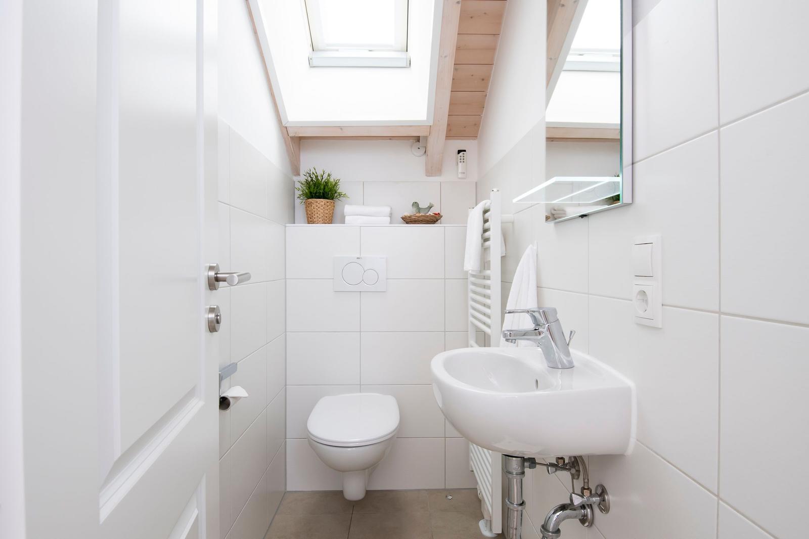 Badezimmer mit Toilette, Waschbecken und Dusche unter Dachschrägen.