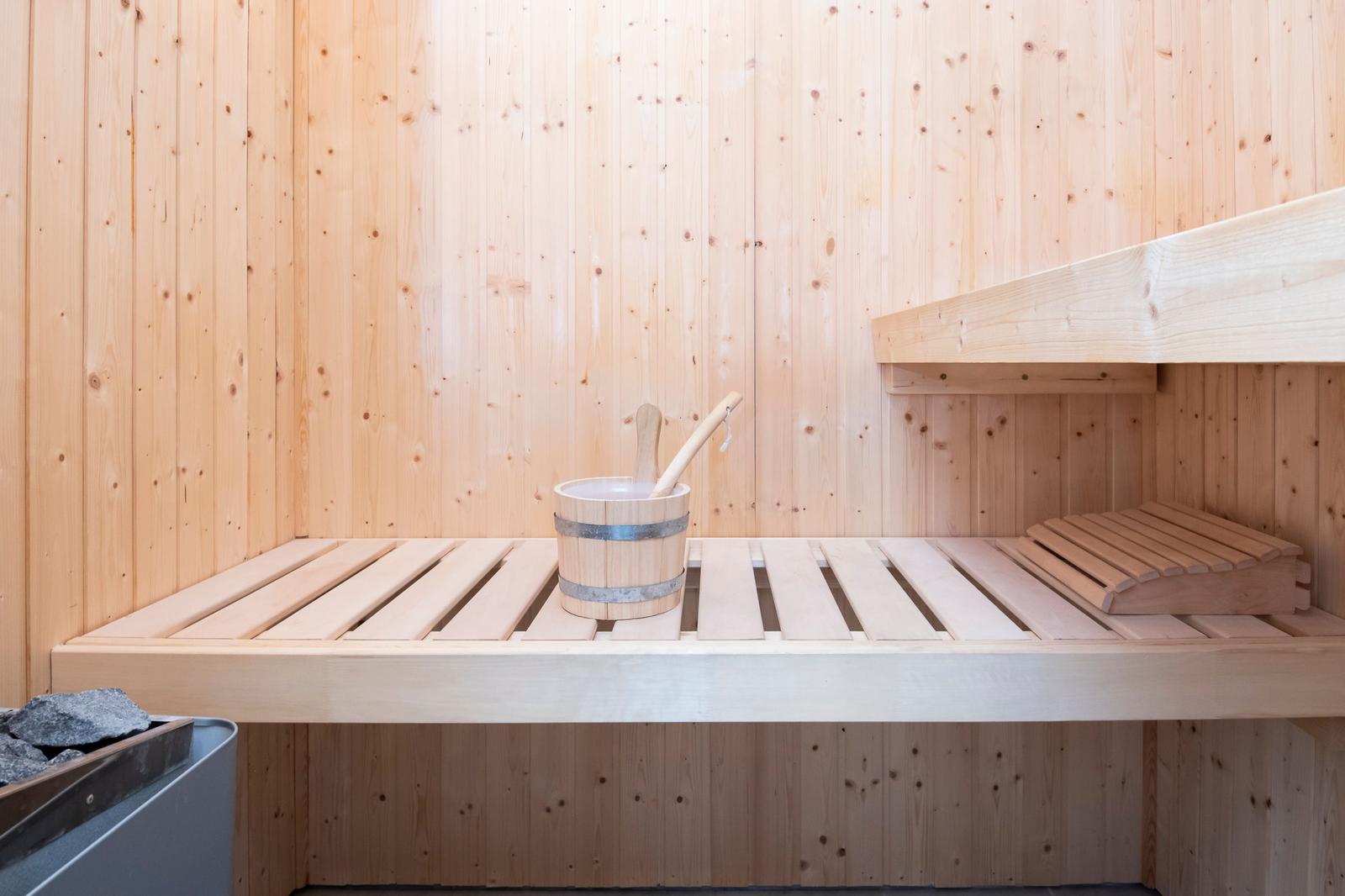 Sauna mit Holzbank, Eimer und Besen. Holzwände und -boden.