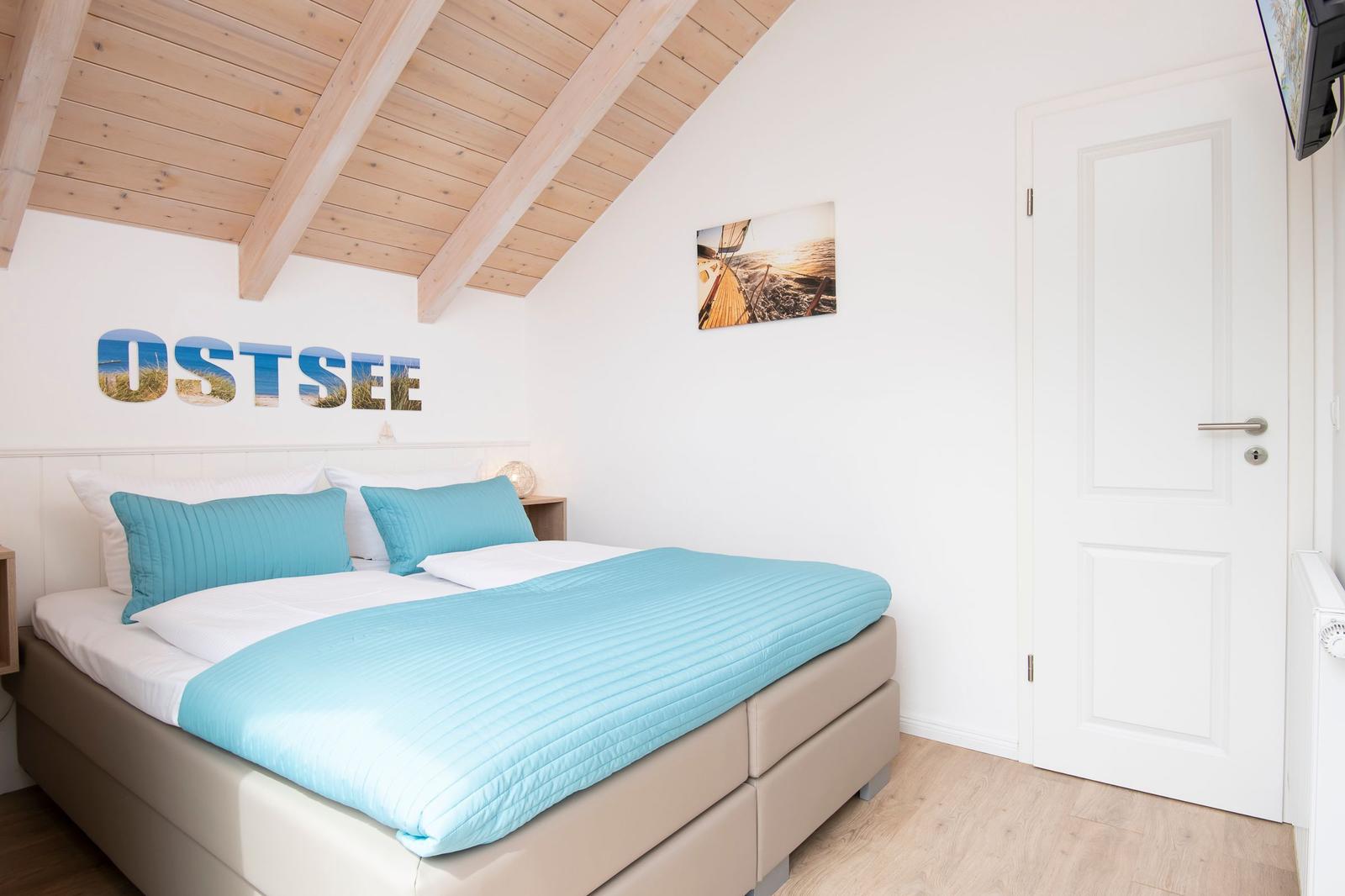 Schlafzimmer mit Bett, Holzdecke und Wandbild. Tür und TV sichtbar.
