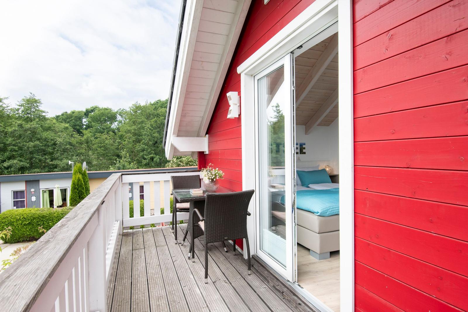 Roter Holzausbau mit Terrasse und Blick in Schlafzimmer mit blauer Bettwäsche.
