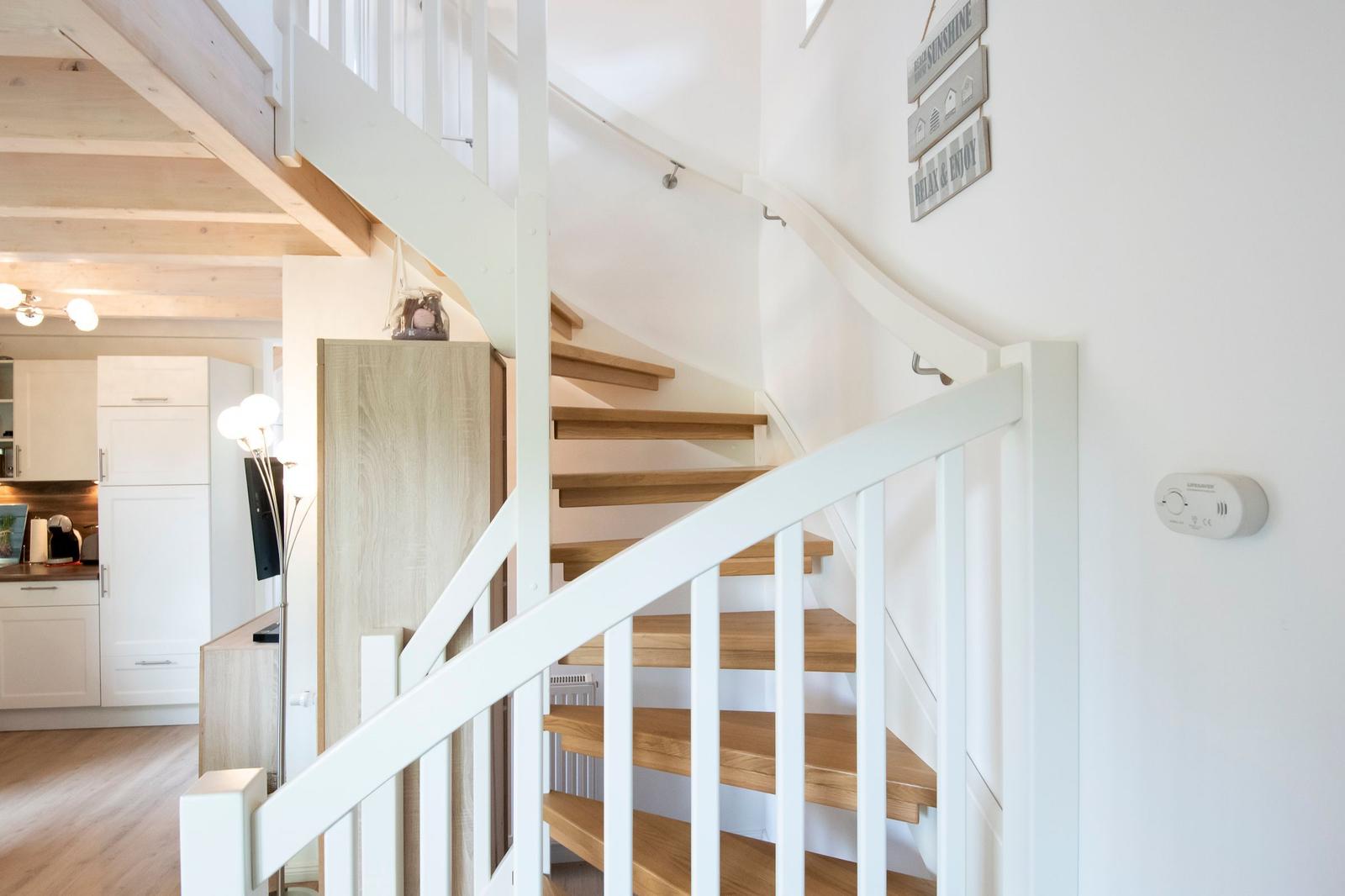 Eine Treppe mit Holzstufen und weißem Geländer führt zur oberen Etage.