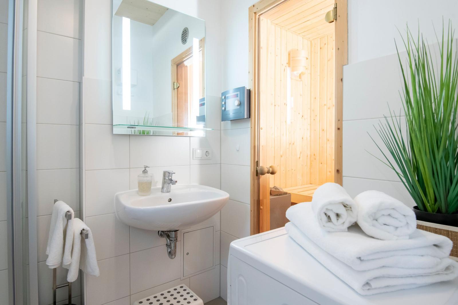 Badezimmer mit Waschbecken, Spiegel, Sauna und Handtüchern.